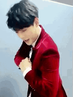 a man in a red suit and tie is standing in front of a wall .
