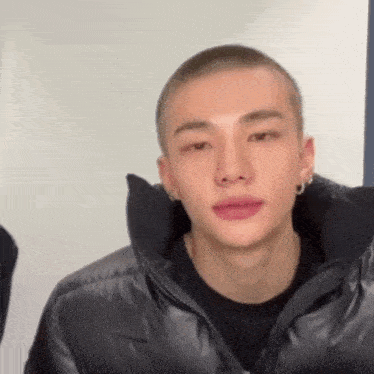 a young man with a shaved head is wearing a black jacket .
