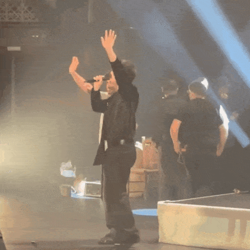 a man in a black shirt stands on a stage with his arms in the air