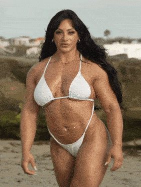 a muscular woman in a white bikini stands on a beach
