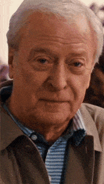 a close up of an older man 's face with gray hair and a striped shirt