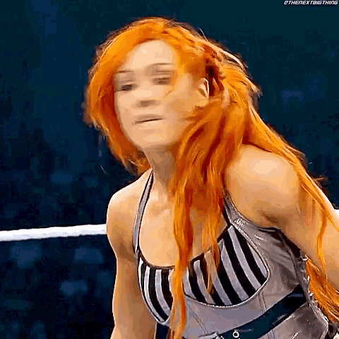 a woman with long red hair is standing in a wrestling ring wearing a striped tank top .