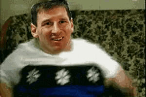 a man is sitting on a couch wearing a white shirt and a blue blanket .