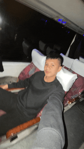 a boy in a black shirt sits in a chair with a white pillow on his head