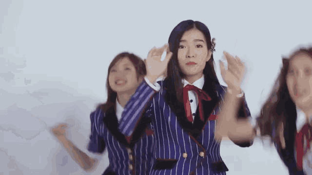 a group of young women in school uniforms are dancing together in front of a white wall .