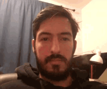 a man with a beard is sitting on a couch in front of a blue curtain