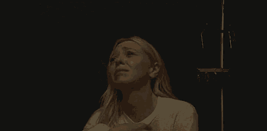 a woman in a white shirt is sitting in a dark room holding a piece of paper