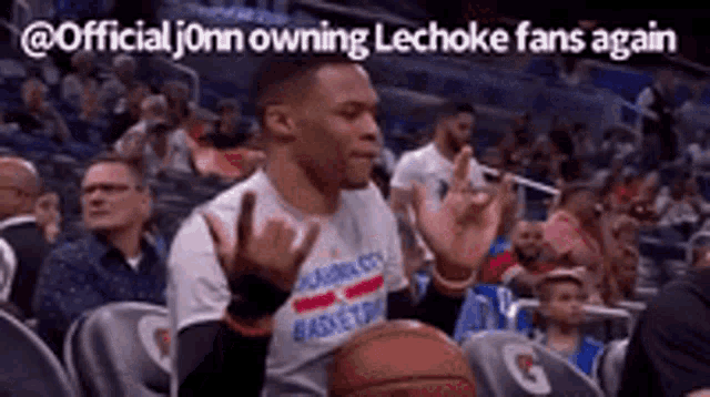 a man is sitting in a stadium with a basketball in his hand and applauding .