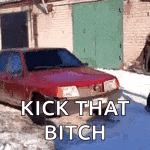 a red car is parked in the snow in front of a building .