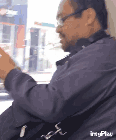 a man wearing glasses is looking at his phone while sitting on a bus