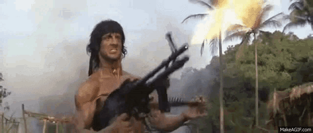 a man is holding a gun in a jungle with flames coming out of the gun .
