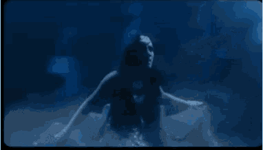 a woman is swimming underwater in a pool with a shark in the background .