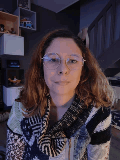 a woman wearing glasses and a colorful sweater smiles for the camera