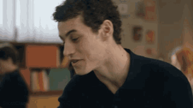 a young man with curly hair is sitting in a classroom talking to someone .