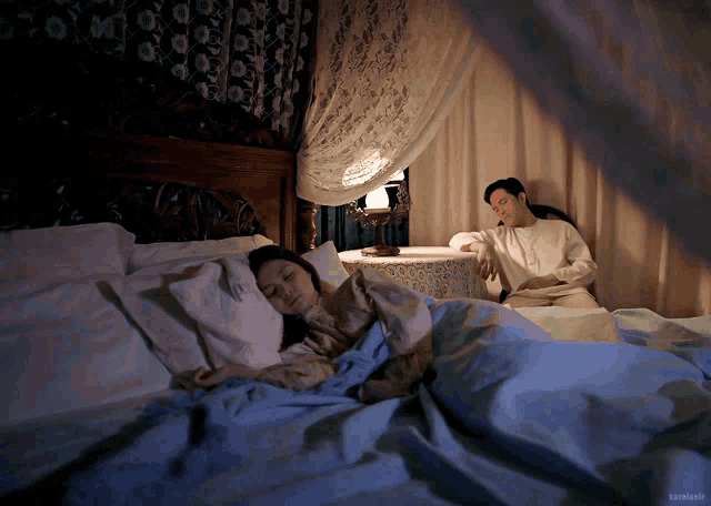 a man sits next to a woman sleeping in a bed with the name kamikaze on the bottom right corner