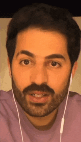 a man with a beard is wearing ear buds and a pink shirt