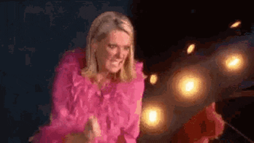 a woman in a pink dress is standing in front of a stage with lights behind her .