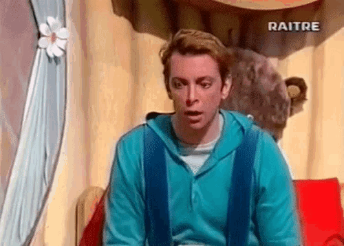 a man in a blue sweatshirt is sitting on a red couch in front of a bear and a sign that says raitre