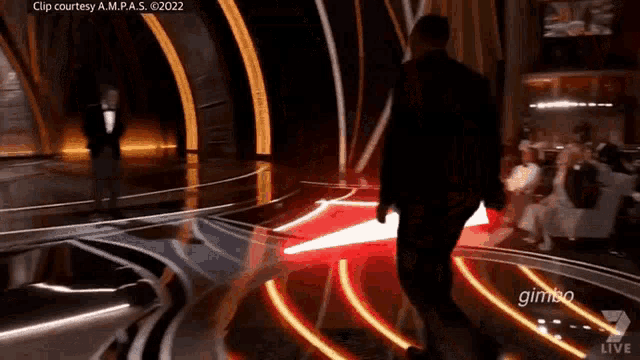 a man in a tuxedo is walking on a stage with a red light behind him .