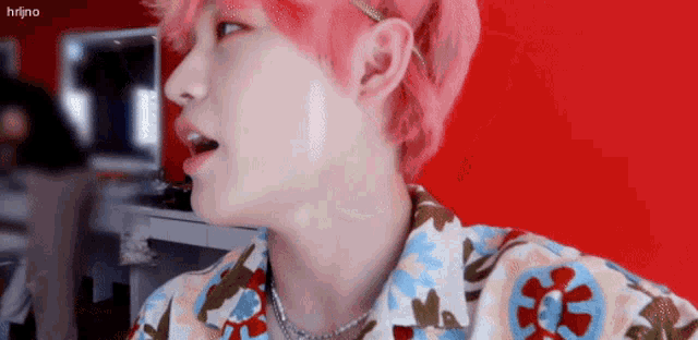 a man with pink hair is wearing a floral shirt and a necklace