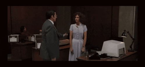 a woman in a white dress stands next to a man in a suit in a dark room