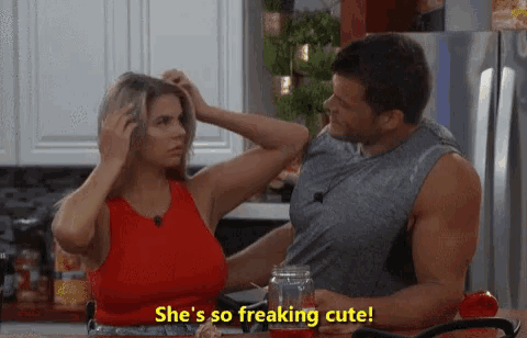a man and a woman are sitting at a table and the woman is saying she is so freaking cute