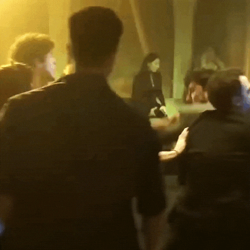 a group of people are standing in a dark room and one of them is wearing a black shirt