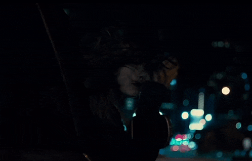 a woman is sitting in a car at night covering her face with her hands .