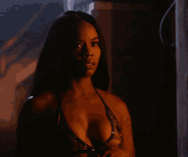 a woman in a very plunging bikini top stands in a dark room