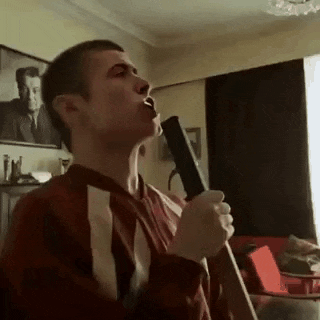 a man is singing into a microphone in a living room while holding a gun .