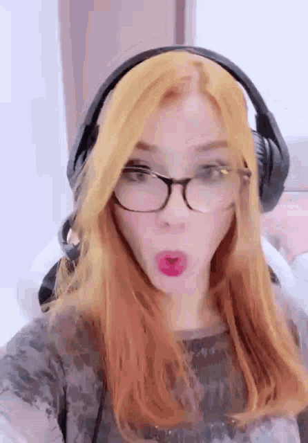 a woman with red hair and glasses is wearing headphones and making a face .