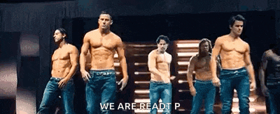 a group of shirtless men are standing on a stage in a line .