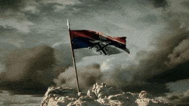 a flag on top of a rocky hill with a cloudy sky