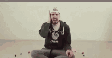 a man wearing a hat and a green hoodie is covering his ears with his hands .