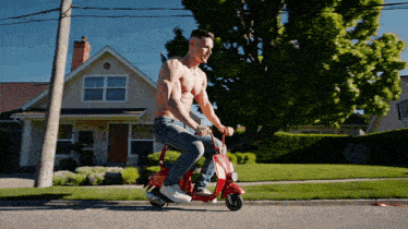 a shirtless man is riding a red scooter on the street