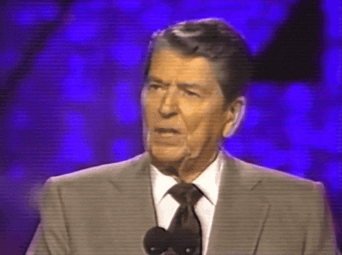 a man in a suit and tie stands in front of a microphone