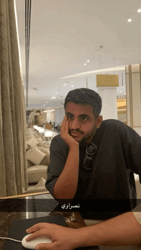 a man is sitting at a table with his hand on his face and a mouse in front of him