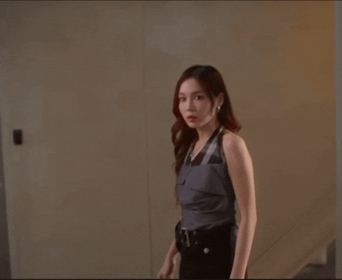 a woman in a gray top and black pants stands in front of a brown wall