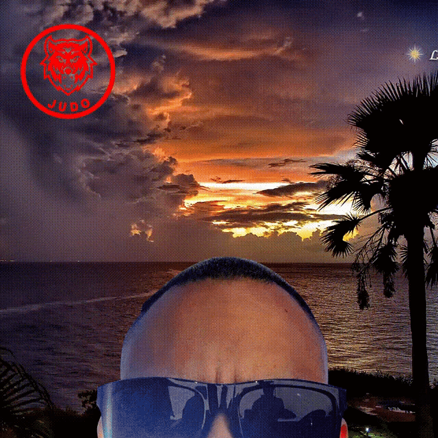 a man wearing sunglasses stands in front of a sunset and the word judo is on the red circle