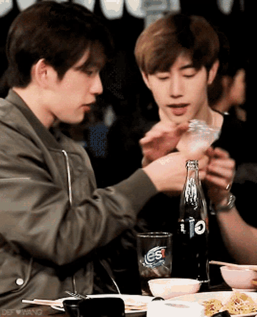 two young men sitting at a table with a bottle of pepsi on it