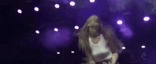 a woman in a white top is dancing on a stage with purple lights