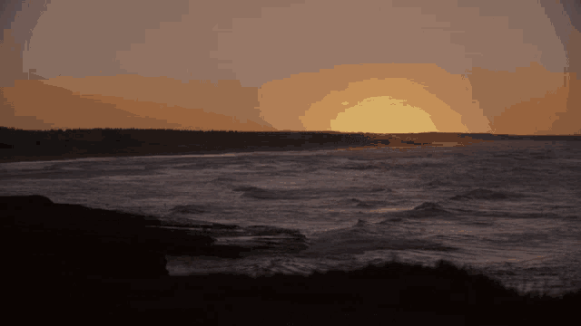 the sun is setting over the ocean with waves crashing on the shore