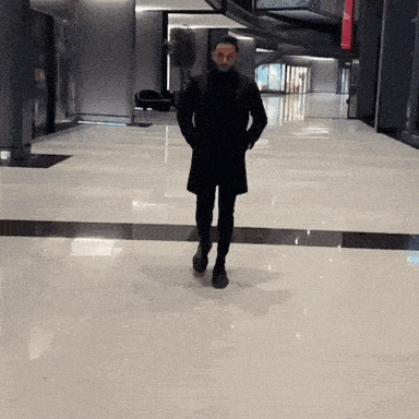 a man in a black coat is walking in a hallway with his hands in his pockets