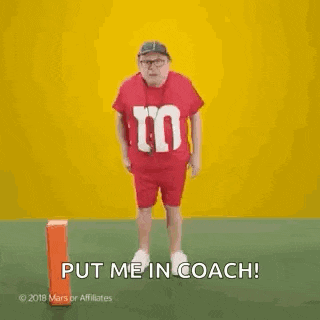 a man in a red m & ms shirt is standing next to an orange block and says `` put me in coach ! ''