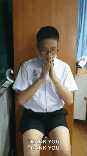 a man in a white shirt and black shorts is sitting in a chair with his hands folded and says thank you