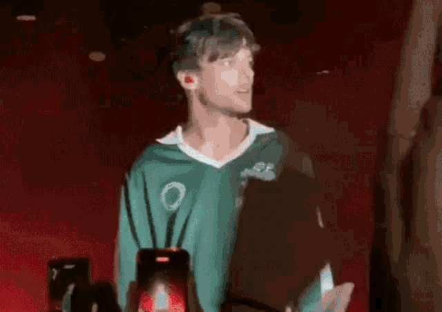 a man in a green jersey is holding a cell phone in front of a red background .