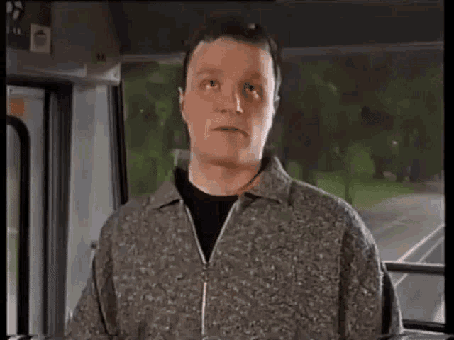 a man is sitting on a bus with his eyes closed and making a funny face .