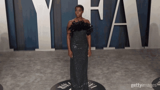 a woman in a black dress stands in front of a vanity fair logo