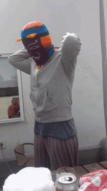 a person wearing a knitted mask stands in front of a window