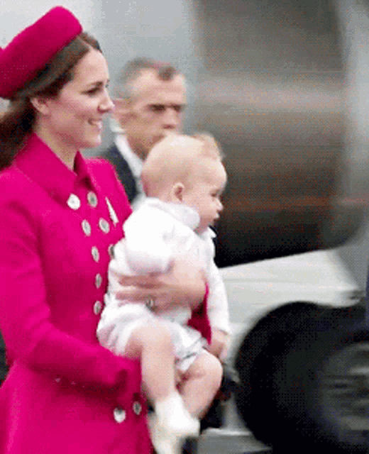 a woman in a red coat is holding a baby in her arms